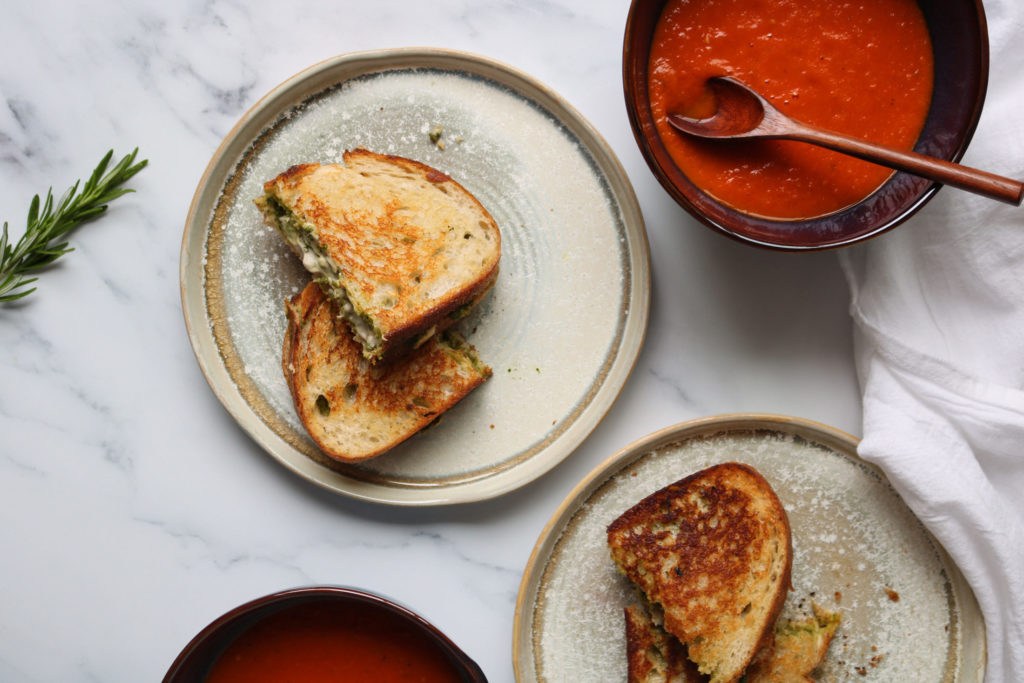 homemade vegan tomato soup in a pot next to vegan pesto grilled cheeze sandwiches on plates