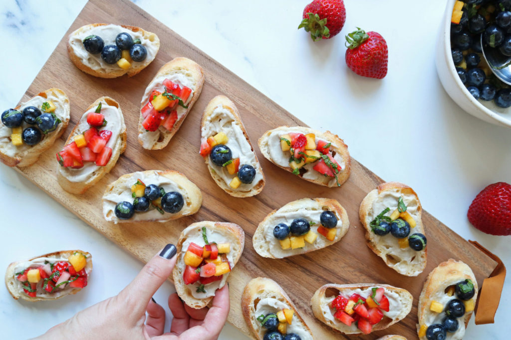 vegan fruit bruschetta piece covered in strawberry and blueberry on a wooden serving tray