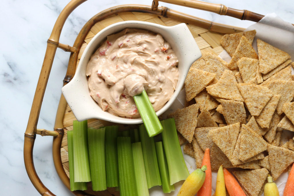 vegan pimento cheese dip on a serving tray surrounded by carrots, celery, and chips