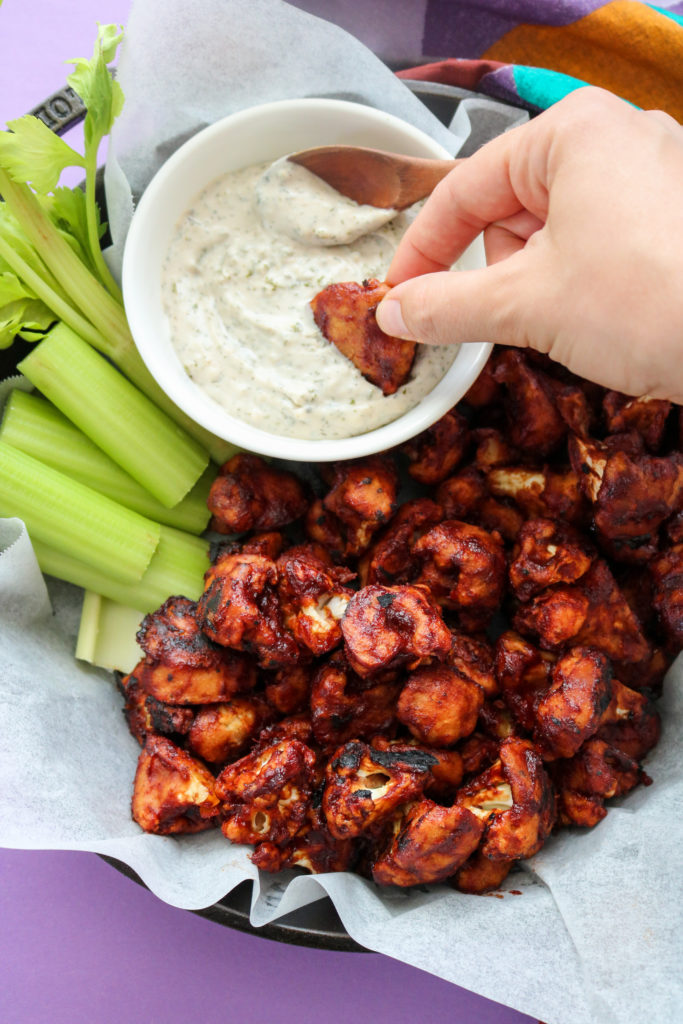 BBQ cauliflower wings being dipped in a bowl of vegan ranch