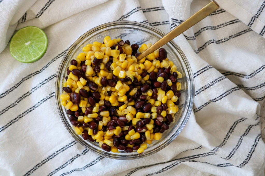black beans and corn in a bowl with a wooden spoon, and a lime on a towel